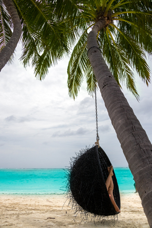 Beautiful woman relaxes on a swing on the dream beachの写真素材