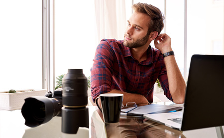Young professional photographer busy scratching the back of his head and looking off to the side thinking about what he is going to shoot nextの写真素材