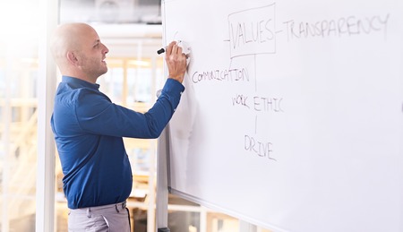 Young caucasian male busy writing on a white board during his presentation about the values he feels...