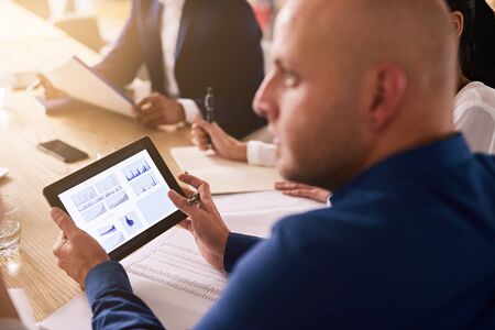 tablet being used in a business meeting with graphs on the display by a caucasian businessman...
