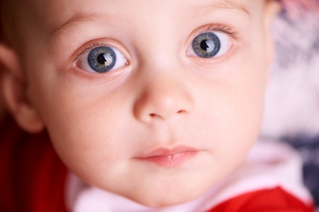 Close up of a beautiful baby boy's face with glowing blue eyes looking straight into the camera with a calm expressionの写真素材