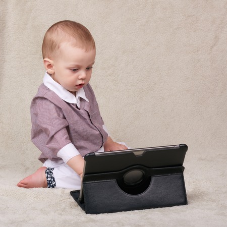 Caucasian baby boy busy using an electronic tablet becoming accustomed to a life surrounding him...