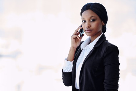 Young attractive, well dressed black businesswoman looking at camera with a serious facial expression while holding her phone against her ear in her right handの写真素材