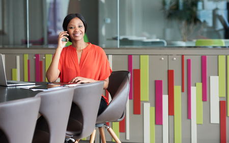 Colourful image of young black businesswoman sitting at a conference table in a modern office space...