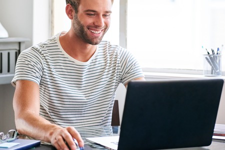 Happy young male student smiling while seated behind his laptopの写真素材