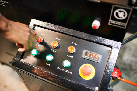 Black hand busy pushing red button on an industrial looking panel of switches for a coffee roasting machineの写真素材