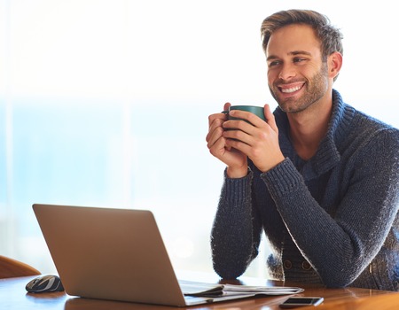 Handsome young caucasian man, happily smiling while holding his coffee mug for warmth in the...