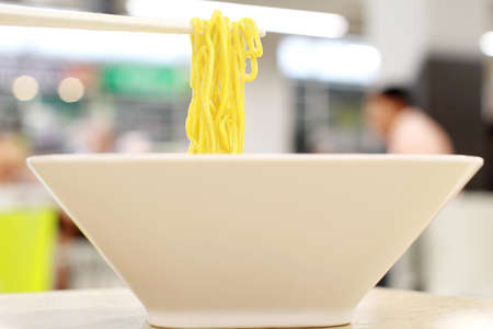 Asian women eating noodles for lunch in the food court., Use a stick to eat hot traditional Chinese...