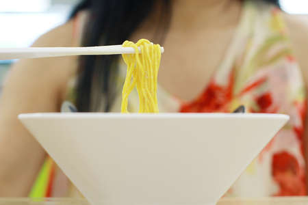 Asian women eating noodles for lunch in the food court., Use a stick to eat hot traditional Chinese food.の写真素材