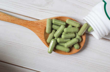 Andrographis paniculata capsule in wooden spoon on wooden background., Herbal extract medicine tablets pills.の写真素材