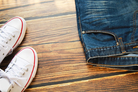 Close-up view of blue jeans and white sneaker on dark old wood background.の写真素材