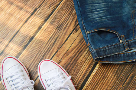 Close-up view of blue jeans and white sneaker on dark old wood background.