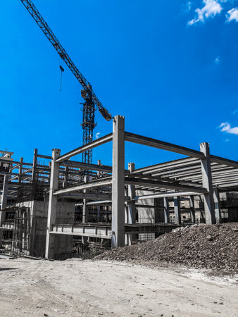 Industrial construction site with cranes and building under construction against blue sky