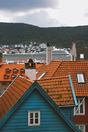 Picturesque view of Bergen. Mountains, clouds, cityscape, wooden houses with tiled roofs, cruise ship. Hordaland, Norway.の写真素材