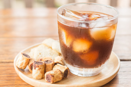 Glass of black iced coffee with some snack, stock photo