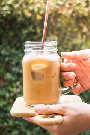 Hand on glass of iced milk coffee with vintage filter effect, stock photo