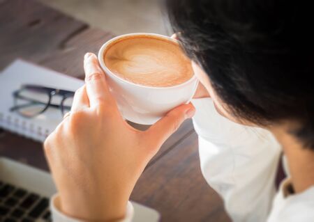 Hand on cup of coffee at work table, stock photo