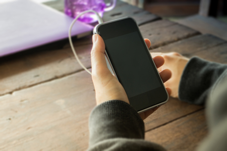 Woman hand on smart phone on wooden table, stock photoの写真素材