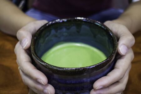 Hand on bowl of hot matcha green tea drink, stock photoの写真素材