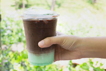 Female hand holding iced coffee drink in disposable take away cup, stock photoの写真素材