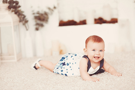Beautiful little baby girl lies on a light carpet in the roomの写真素材