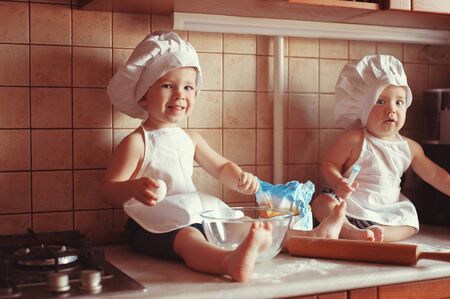Two little boys cook play dough on the table in an apron and chef's hatの写真素材