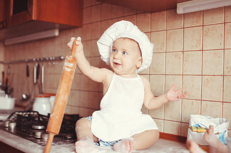 Little scullion is kneading dough in an apron and chef's hat sitting in the flour.の写真素材