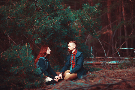 The red-haired guy with a beard and curly red-haired girl on the background of fabulous scenery of nature. Beautiful loving couple on a walk in the woods.の写真素材