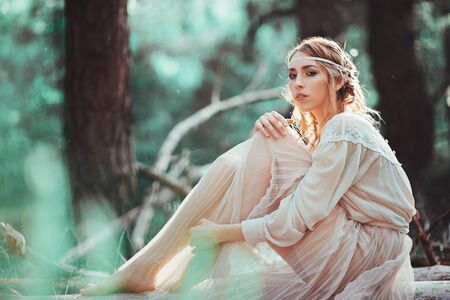 Beautiful artistic photo ginger girl in white dress sitting on the ground in the woodsの写真素材