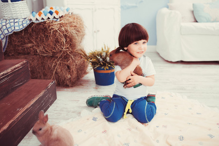 The little dark-haired boy playing in a room with a real rabbitの写真素材