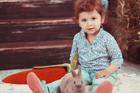 The little red-haired girl playing with rabbit in the room. The concept of happiness, joy and family valuesの写真素材