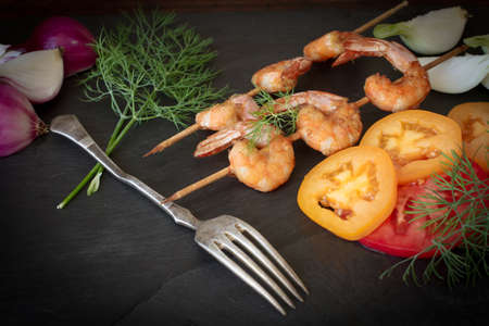 Grilled shrimp with dill tomatoes and onions on a black stoneの写真素材