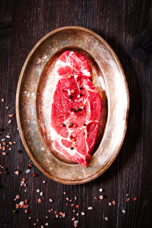 piece of raw meat beef on plate with peppers matelicheskoy on dark wooden backgroundの写真素材