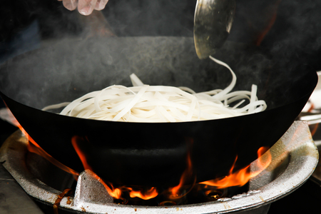 street food. fried noodles in a wok with chicken and shrimp on the open fireの写真素材