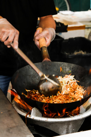 street food. fried noodles in a wok with chicken and shrimp on the open fireの写真素材