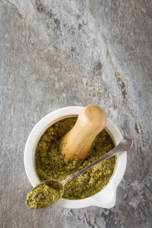 Homemade green pesto sauce with basil and pine nuts in white mortar over gray stone table.の写真素材