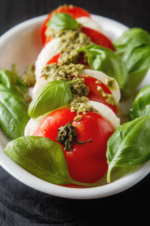 Fresh italian Caprese salad tomato and mozzarella slices with basil leaves green pesto on a blue plate. wooden backgroundの写真素材