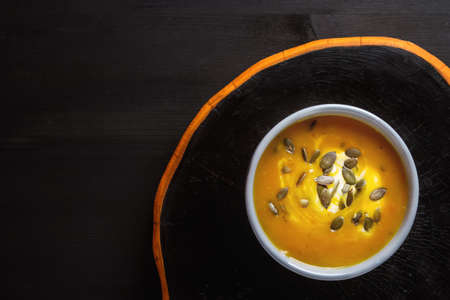Fresh homemade carrot soup with pumpkin seeds and sour cream in a blue vintage plate.の写真素材