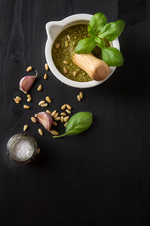 Homemade green pesto sauce with basil and pine nuts in white mortar over old dark wood table.の写真素材