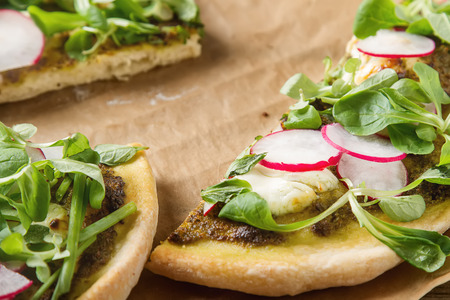 Home Italian pizza with pesto, lettuce and radish on baking paper.  wood background.