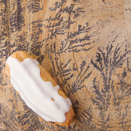 Traditional French cuisine. Eclair drizzled with white icing. Bright stone background