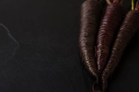 Ripe black carrots. Dark stone background. Autumn harvest.の写真素材