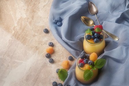 Milk Caramel dessert in a glass jar with berries. Bright stone background, blue clothの写真素材