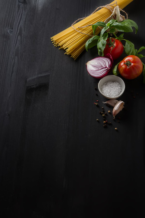Ingredients for cooking pasta Bolognese. Spaghetti, Parmesan cheese, tomatoes, garlic, basil on a black concrete backgroundの写真素材