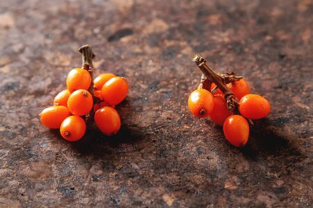 Fresh sea buckthorn on a branch lying on  plate, juice. Dark wood background