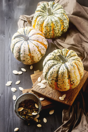 Halloween symbol. Ripe pumpkins from the farm on the wooden board dark fabric, seeds. Black backgroundの写真素材
