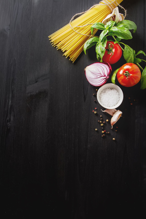 Ingredients for cooking pasta Bolognese. Spaghetti, Parmesan cheese, tomatoes, garlic, basil on a black concrete backgroundの写真素材