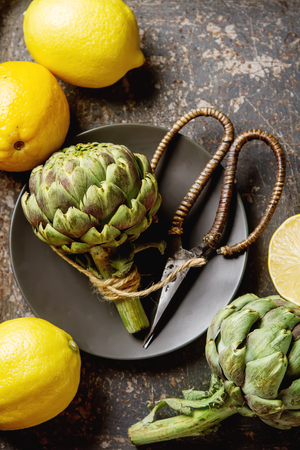 Baby ripping organic Artichokes in the rustic wooden board with lemon, solfetka. Dark backgroundの写真素材