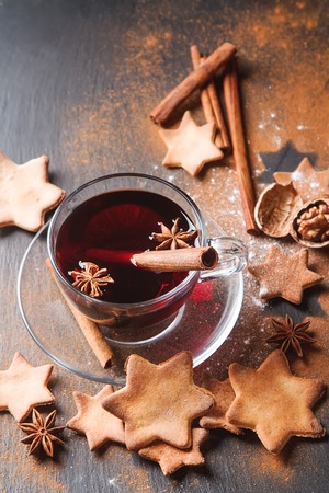 Hot mulled wine in a glass with orange slices, anise and cinnamon sticks, star cookies on vintage wood table. Christmas or winter warming drink with recipe ingredients aroundの写真素材