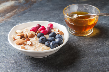 Home oatmeal with cranberries and blueberries. White plate, honey. Dark background. A delicious, healthy breakfastの写真素材